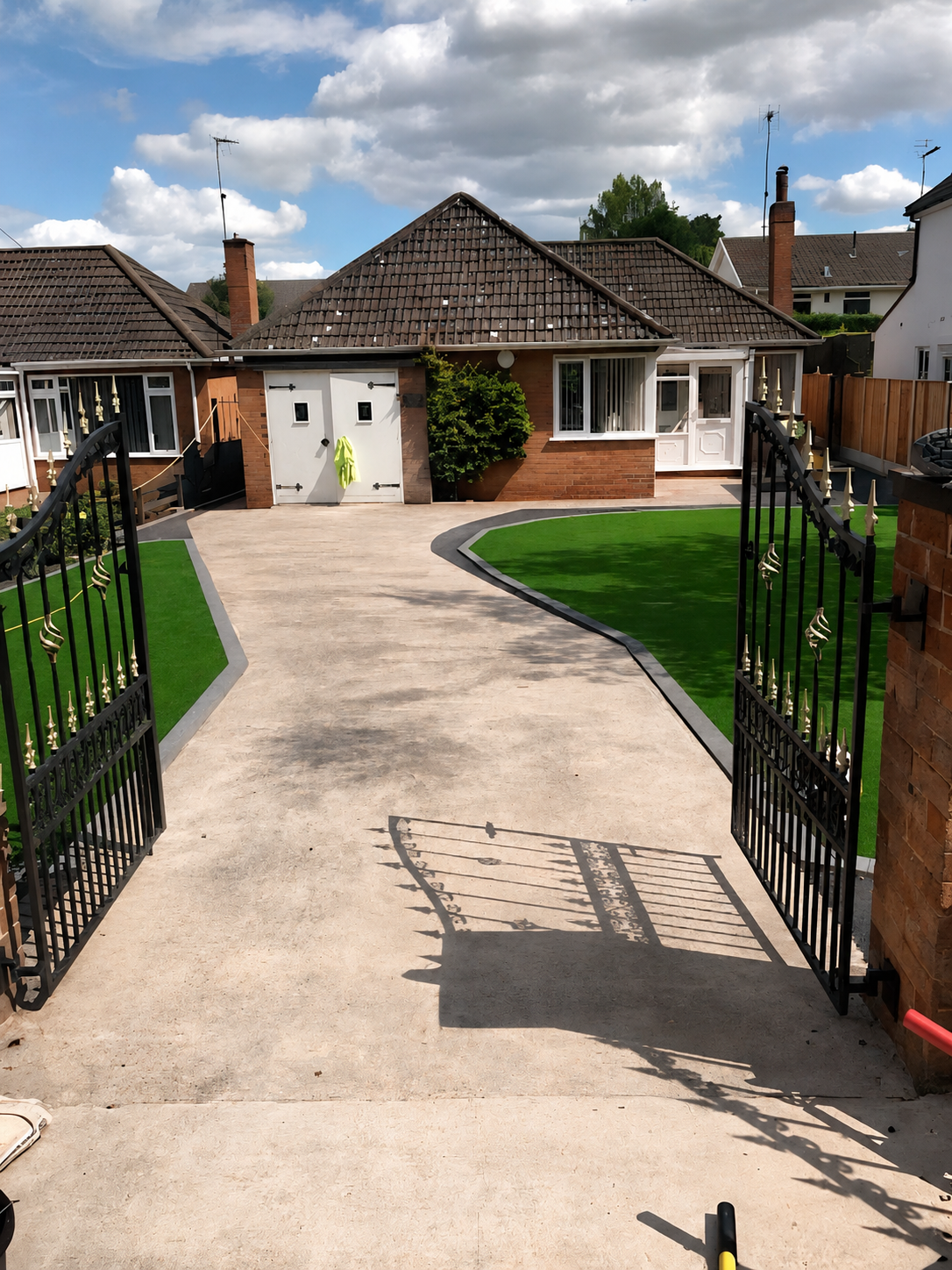 Resin bound driveway looking down towards a white bungalow with the black wrought iron gates open